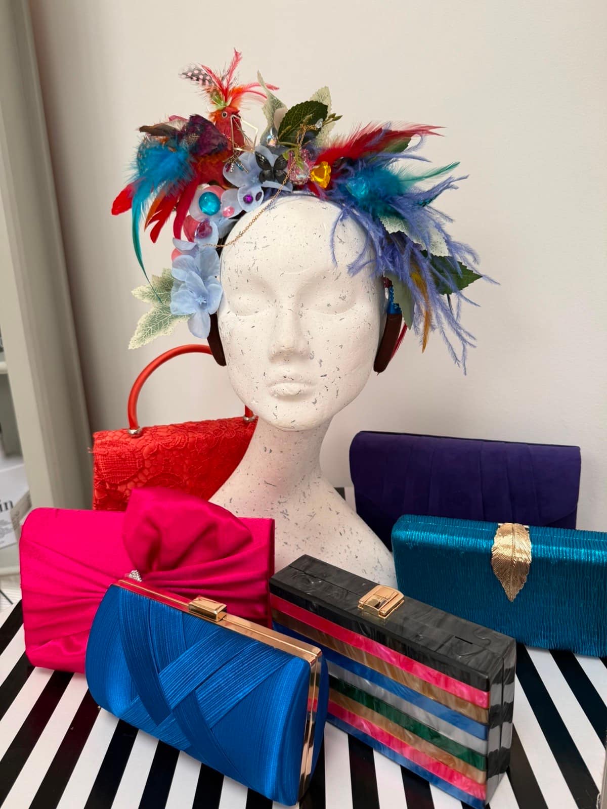 Multicoloured feather and jewel headband crown with butterflies, displayed with pink, blue, teal and striped clutches