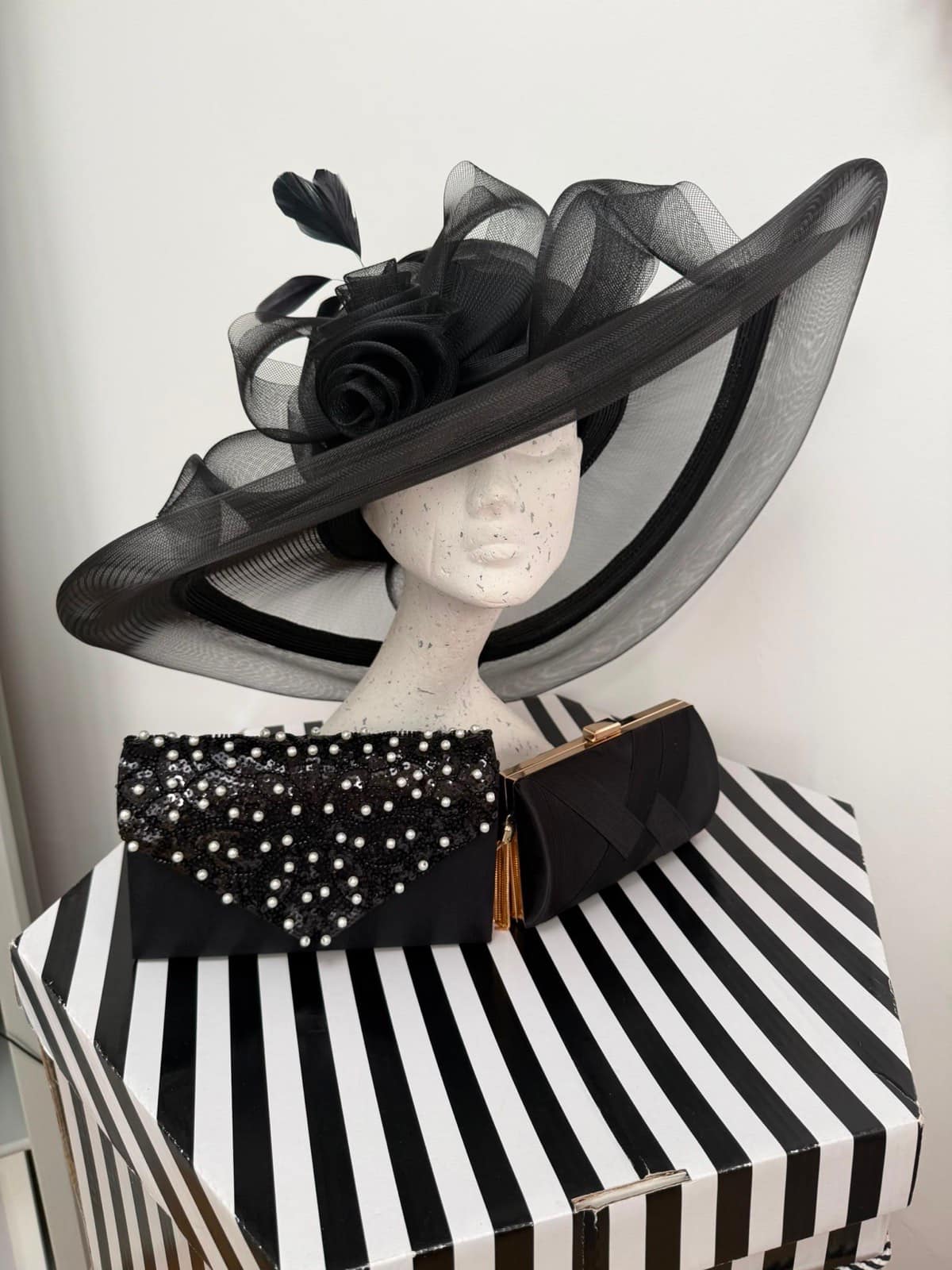 Sheer black crin wide-brim hat with a rose and feather trim, shown with pearl-beaded and pleated black clutches