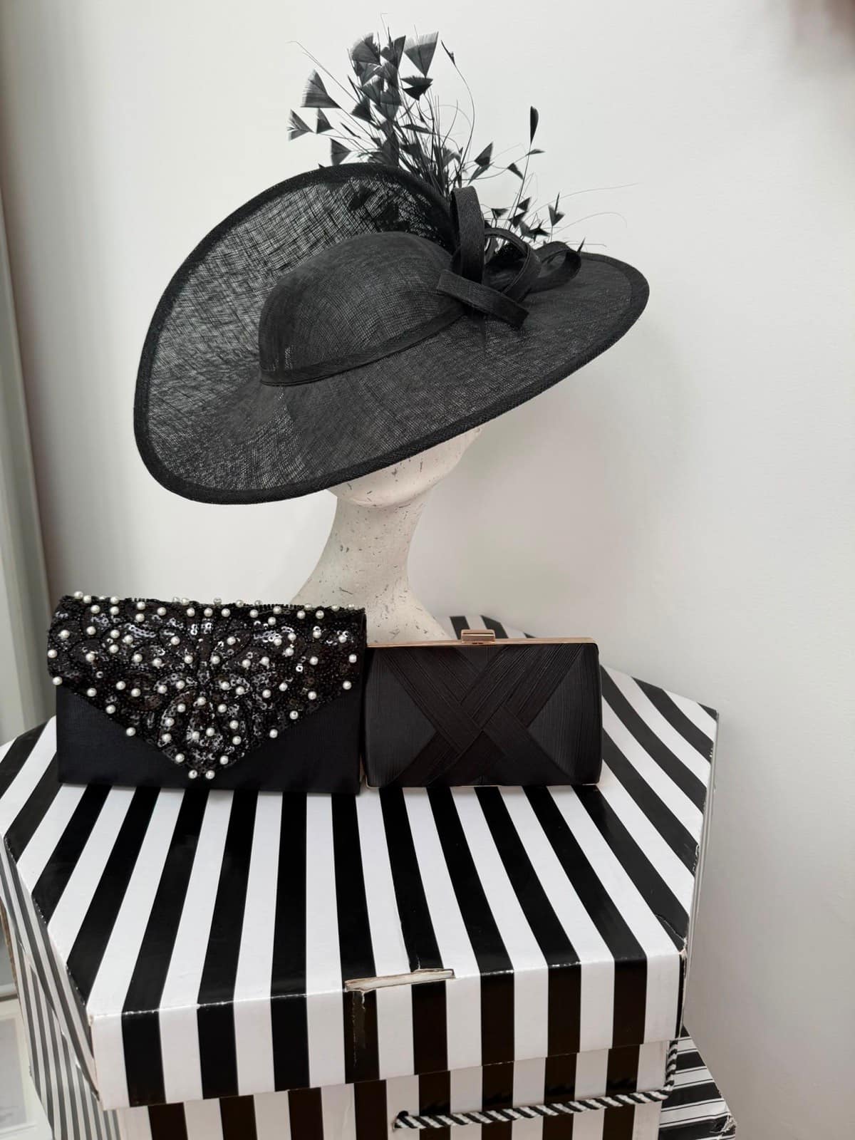 Black domed saucer hatinator with tall feather plumes, displayed with two black clutches