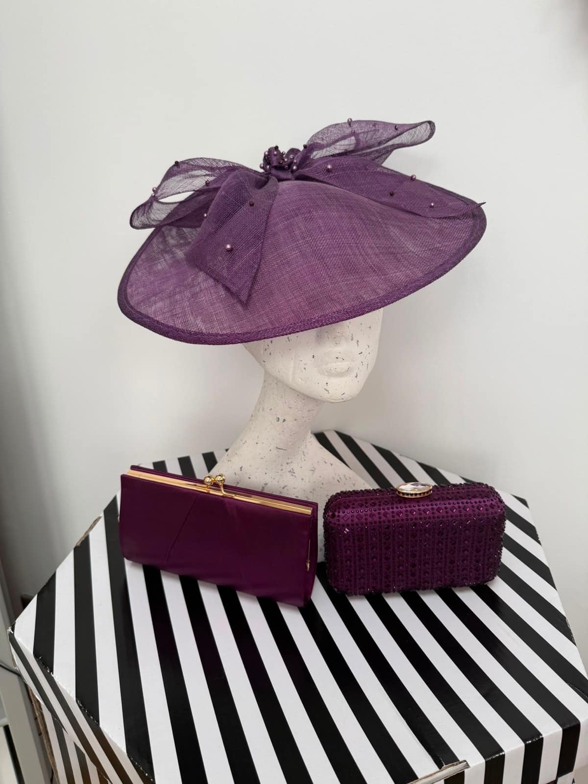 Aubergine saucer hatinator with a pearl-studded crin bow, plum frame clutch and jewelled box clutch