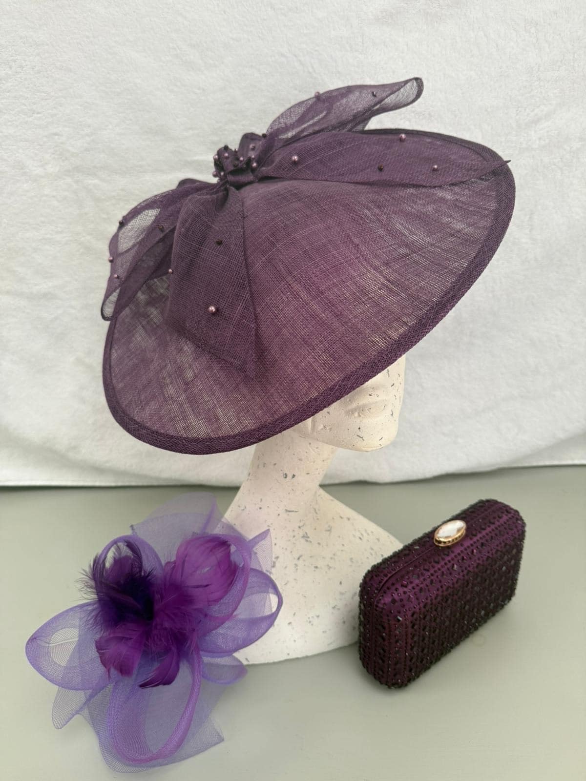 Plum saucer hatinator with beaded bow, purple feather fascinator and jewelled plum clutch