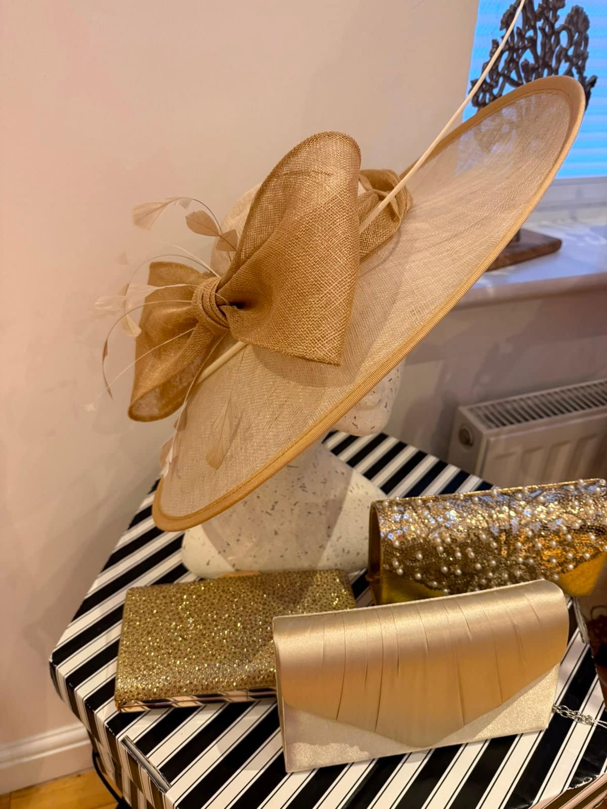 Champagne and gold hatinator with a large sinamay bow and feathers, with four gold occasion clutches