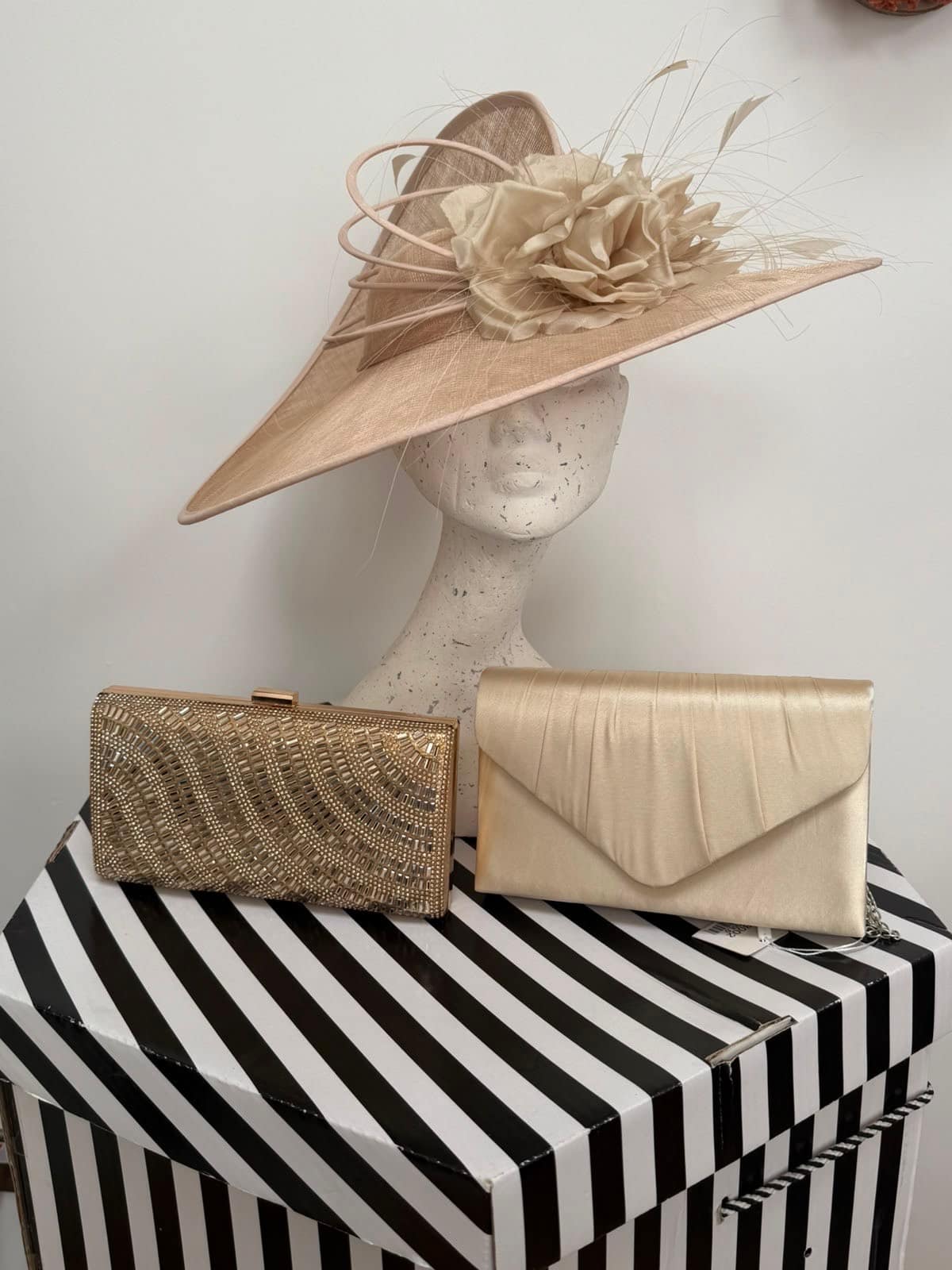 Cream occasion hat with a sweeping organza bow, displayed with three gold clutch bags